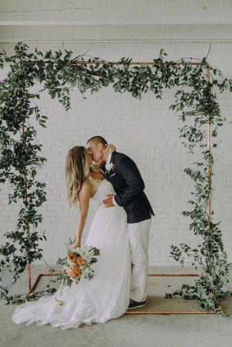 sage green wedding greenery arch groom and bride kissing at the ceremony autumn berrier