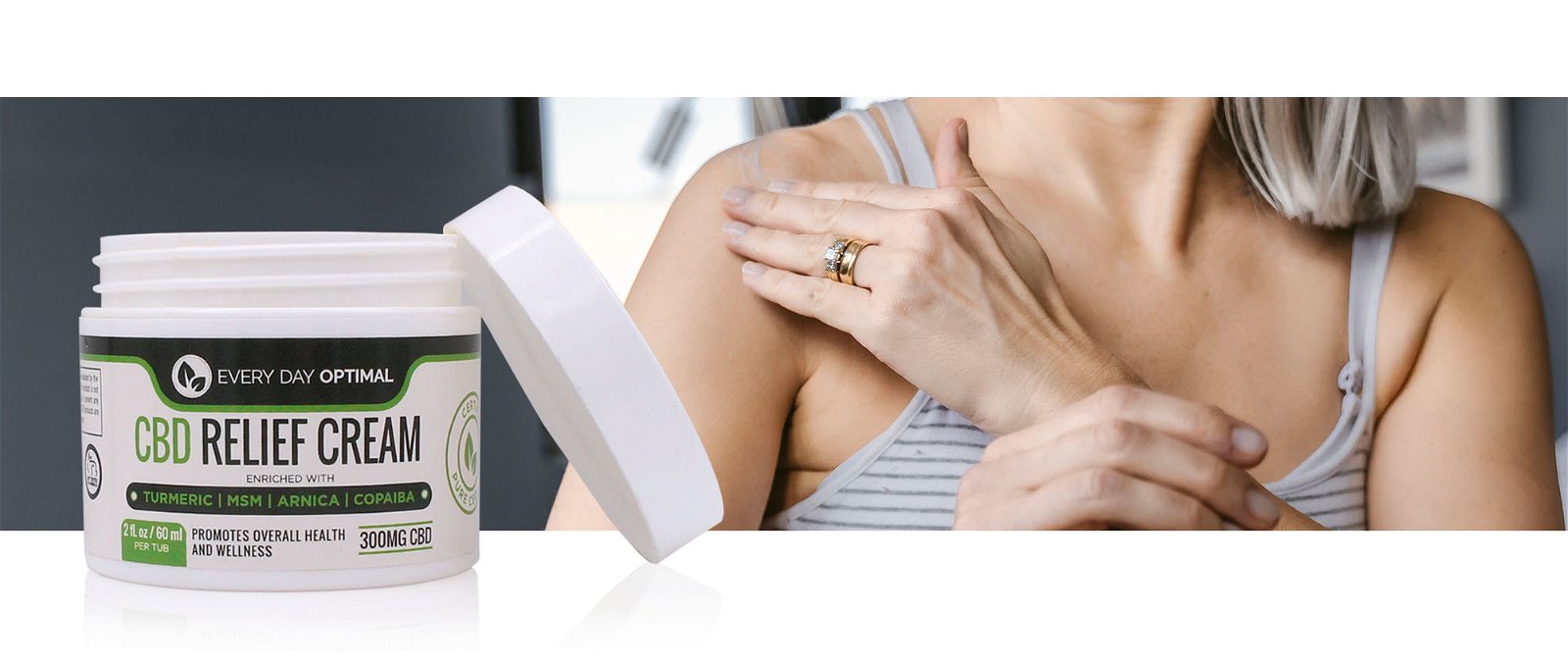 A bottle of CBD relief cream is sitting in front of a silver haired woman putting the cream on her shoulder