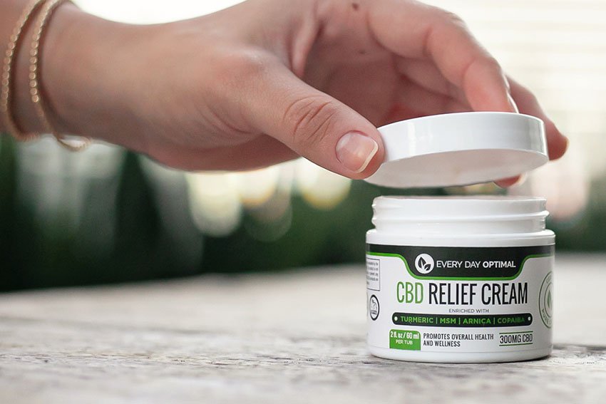 A hand reaching out to open a bottle of CBD relief cream