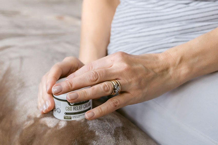 Woman getting some CBD relief cream about of a bottle of CBD relief cream