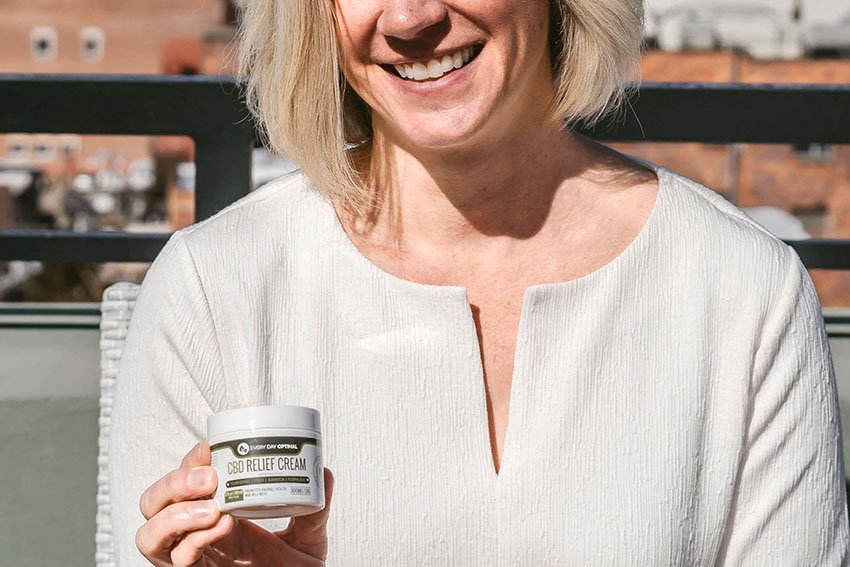 Woman smiling and holding out a bottle of CBD relief cream