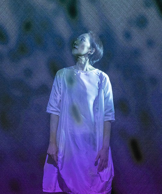 A photograph of a woman dressed in white with a blue-ish purple light over her.