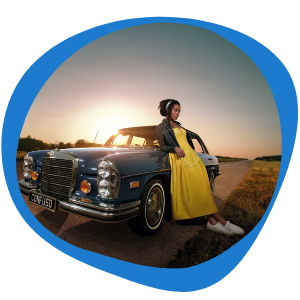 A woman in a yellow dress leaning against a car watching the sun set