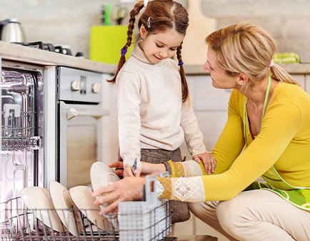 Mom and daughter taking dishes out from dishwasher.