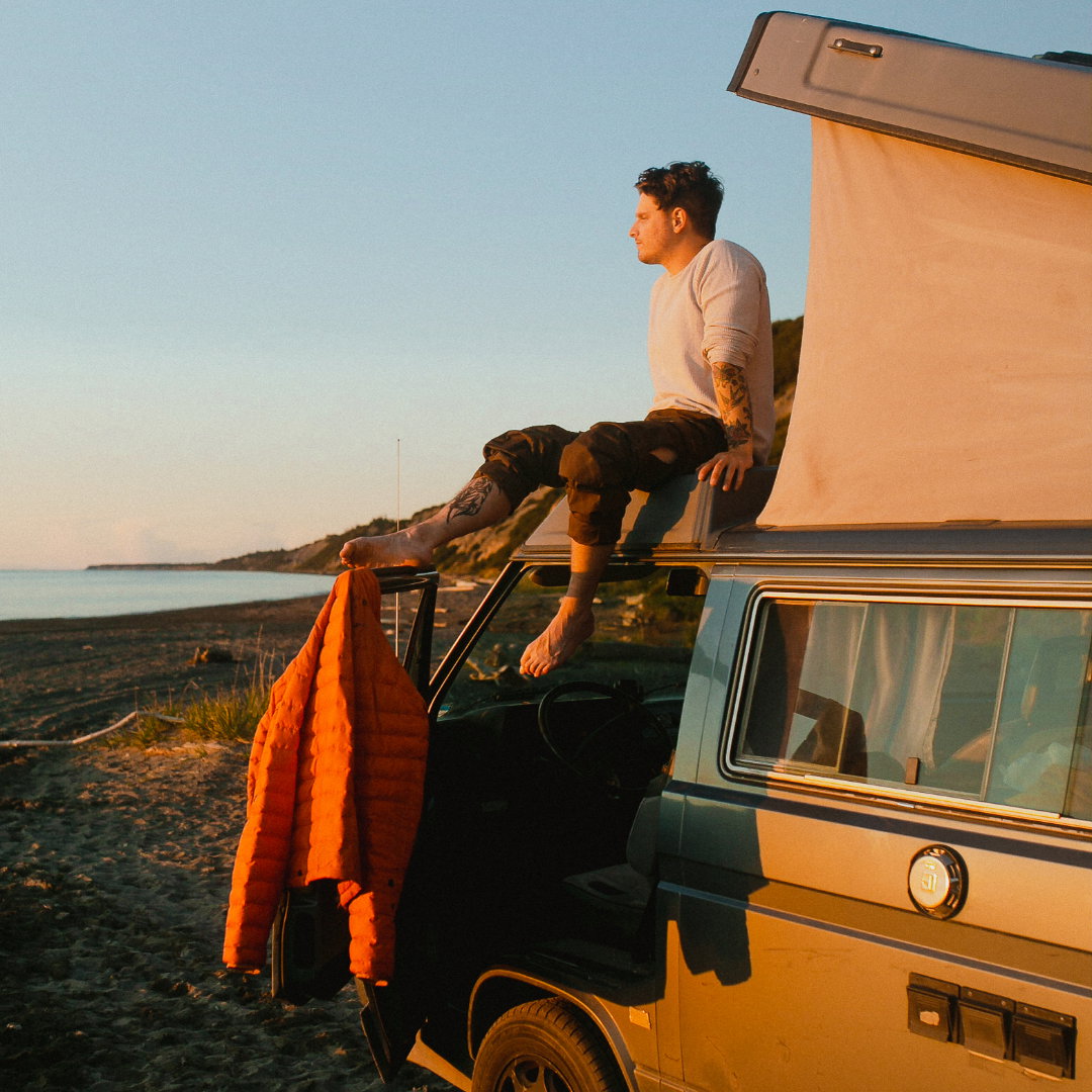 man sitting on top of his van on beach