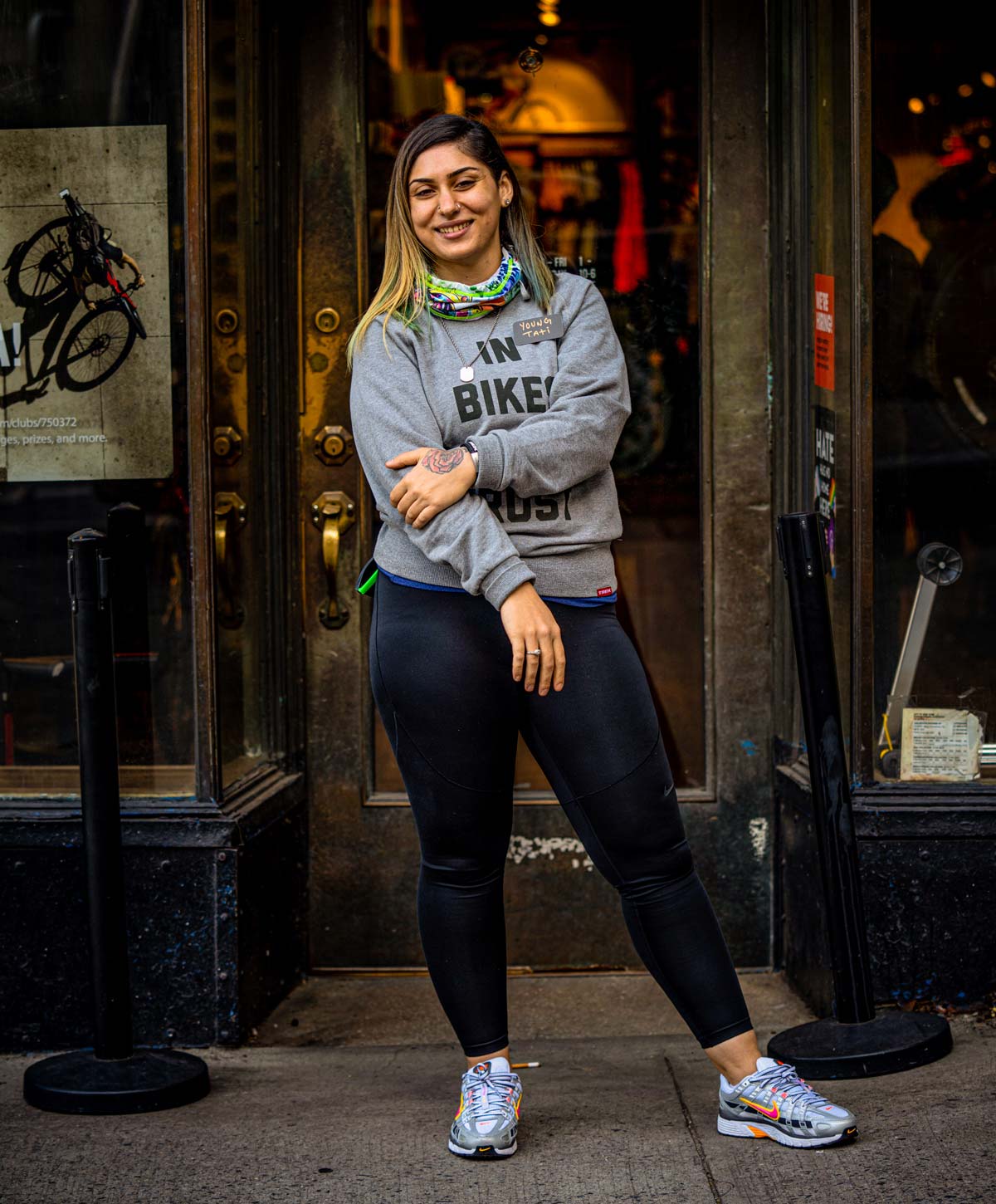 Tati Koufopanteli wearing a gray sweatshirt and leggings standing in front of a the front door of a local bike shop