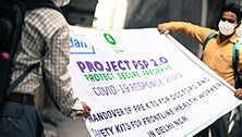 Zwei Arbeiter verpacken ein Werbeplakat, das auf die Verteilung von persönlicher Schutzausrüstung für medizinisches Personal in Neu-Delhi aufmerksam macht.