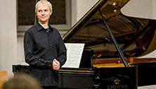 Pianist und Komponist Roland Vossebrecker steht vor einem Flügel. Innerhalb von sechs Jahren hat er mit Benefiz-Konzerten 100.000 € Spenden für Oxfam eingesammelt.