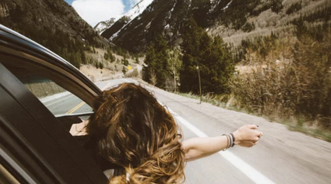 Girl enjoying driving through mountains in car