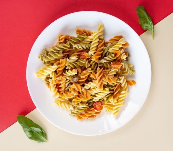Top-down view of delicious-looking tricolored fusilli pasta in a white bowl, garnished by two basil leaves