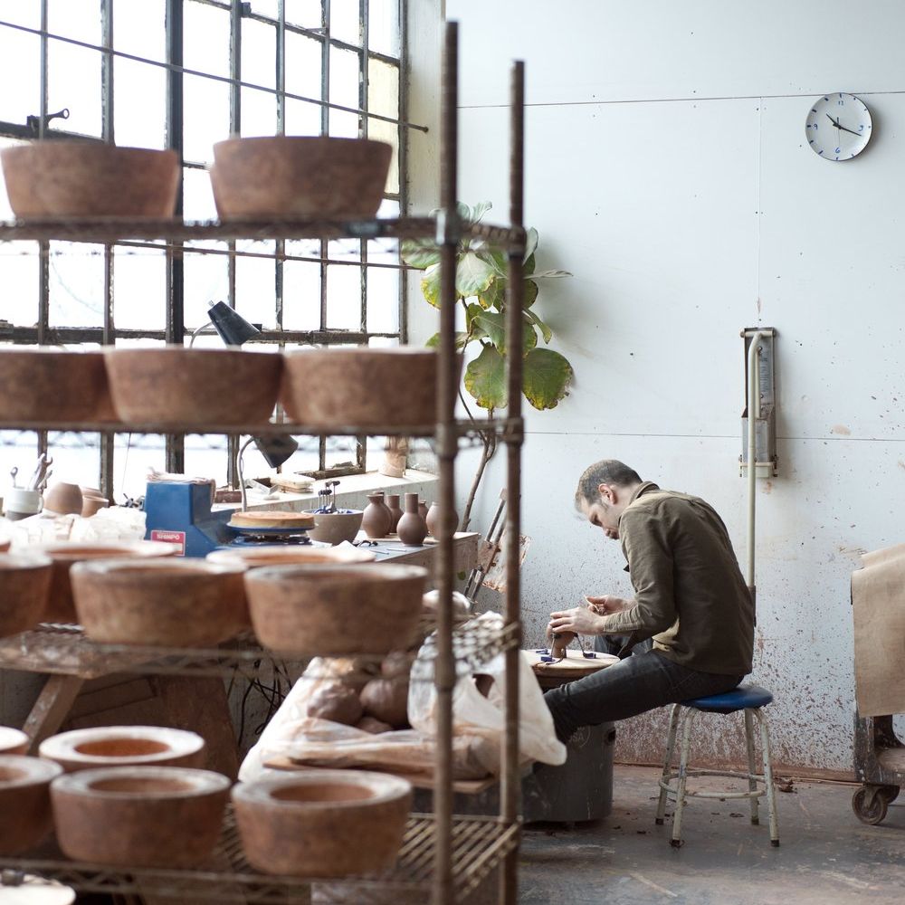 Ceramicist sitting in front of a large window with clay pots