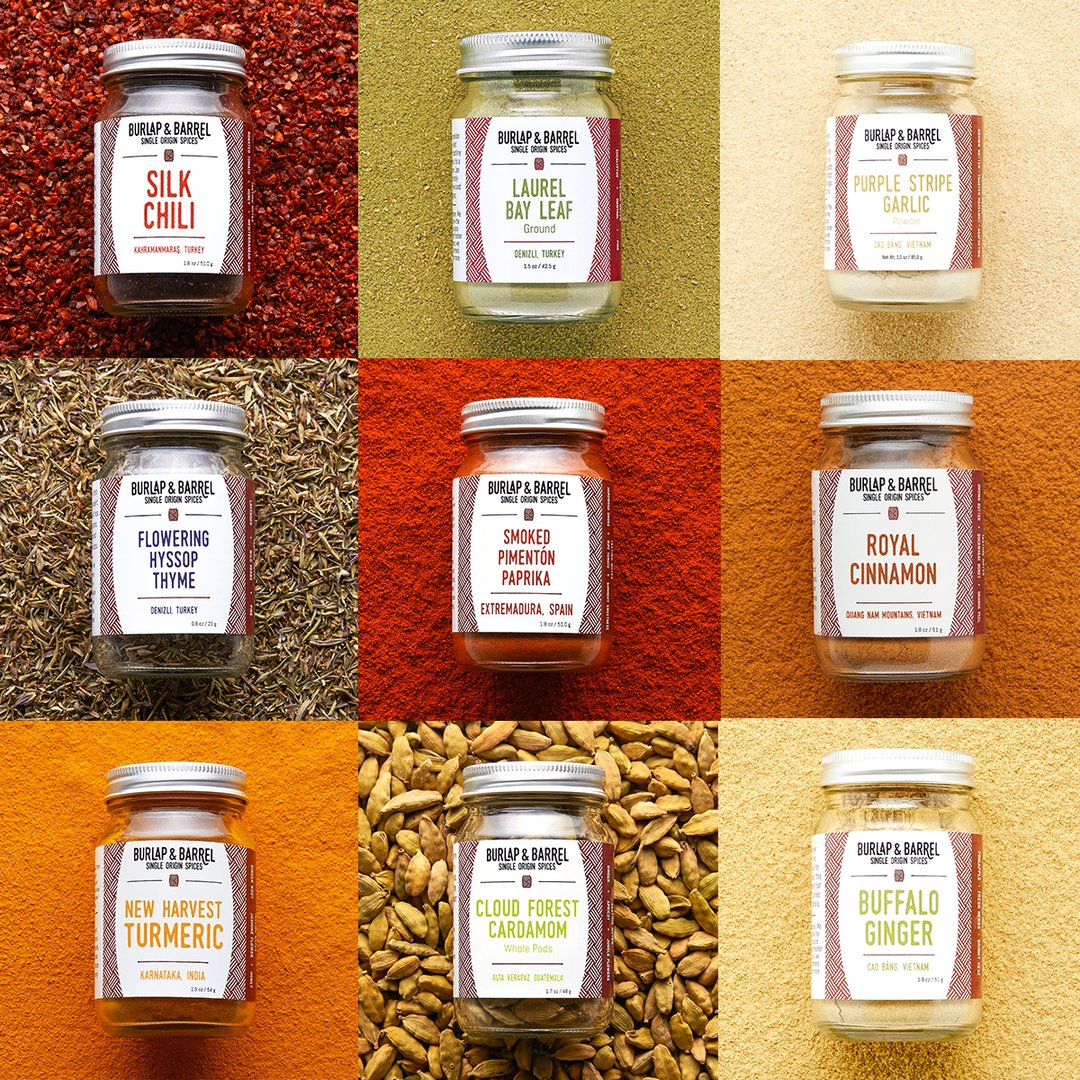 A 3 by 3 grid of jars of spices. The top row has glass jars of Silk Chili, Laurel Bay Leaf and Purple Stripe Garlic. The second row has Flowering Hyssop Thyme, Smoked Pimenton Paprika and Royal Cinnamon. The third row has New Harvest Turmeric, Cloud Forest Cardamom and Buffalo Ginger.