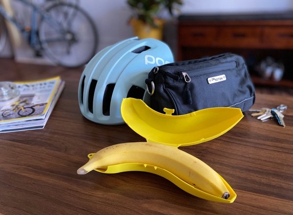 Image of banana in banana protector on table with bike bag and bike helmet.