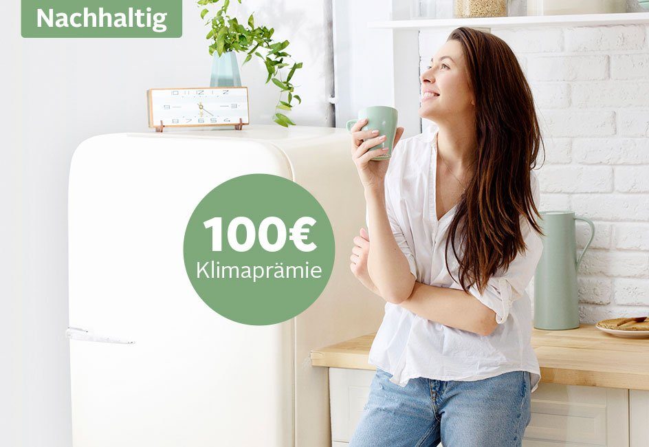 Frau lehnt an der Küchenzeile und hält einen Kaffeebecher in der Hand