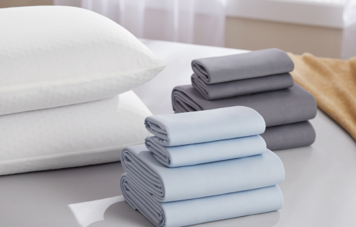A stack of two Harmony Pillows and two sets of folded SoftStretch sheets.