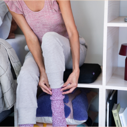 A Woman putting on socks while sitting on a Purple seat cushion.