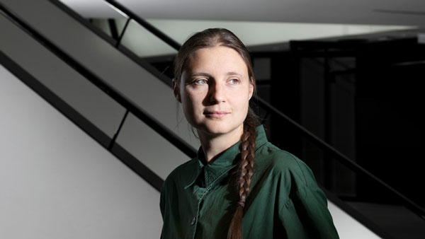 Maryna Viazovska stands in front of a spare black-and-grey background, with her face illuminated from the side and her plait hanging over her shoulder.