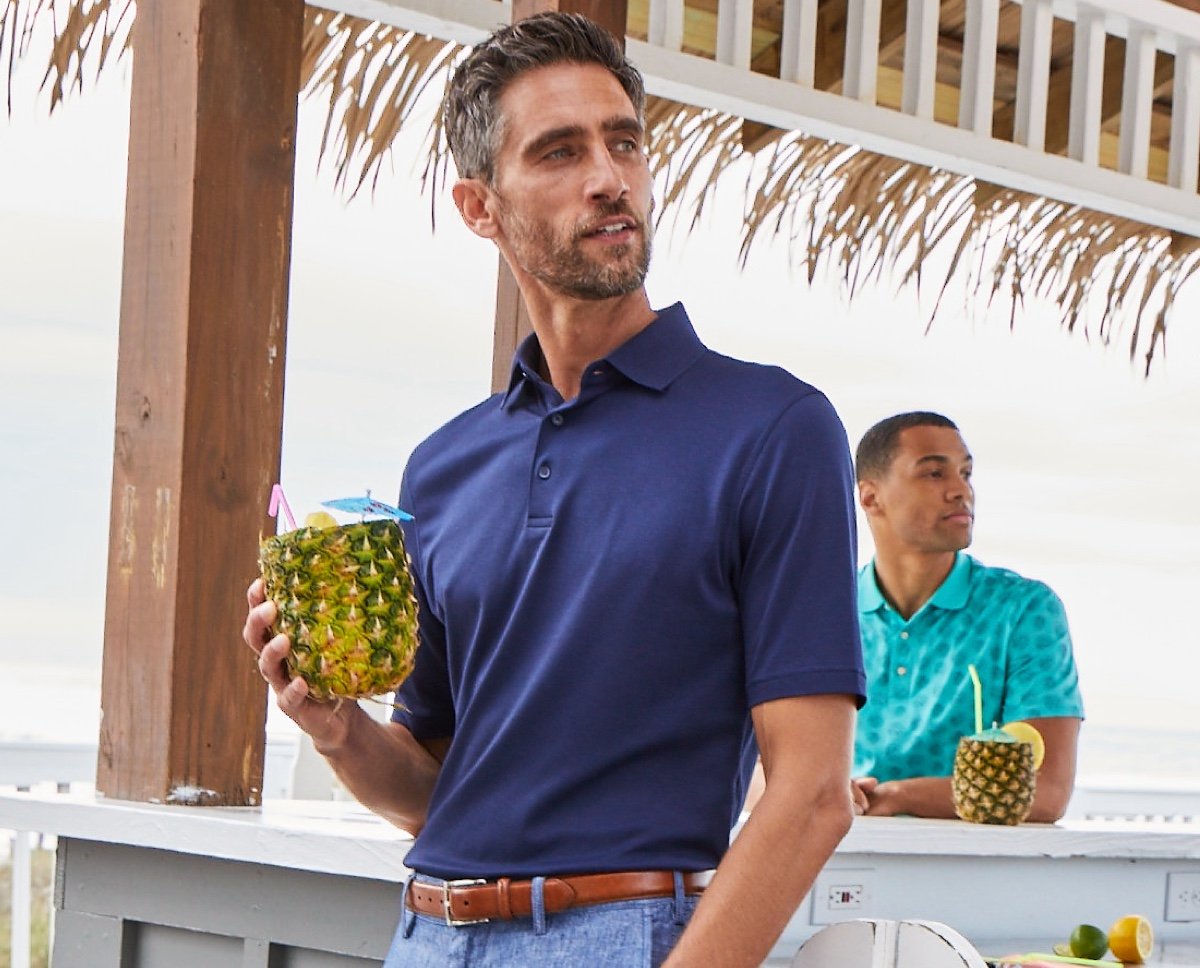 Man in dark blue polo leaning against an outdoor bar