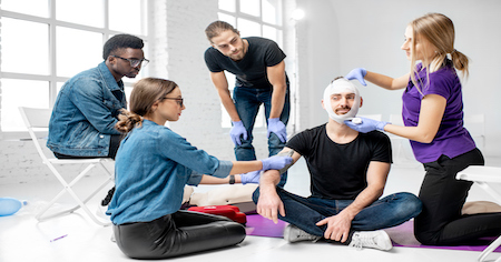 Verschiedene Menschen üben Handgriffe im Erste Hilfe Kurs