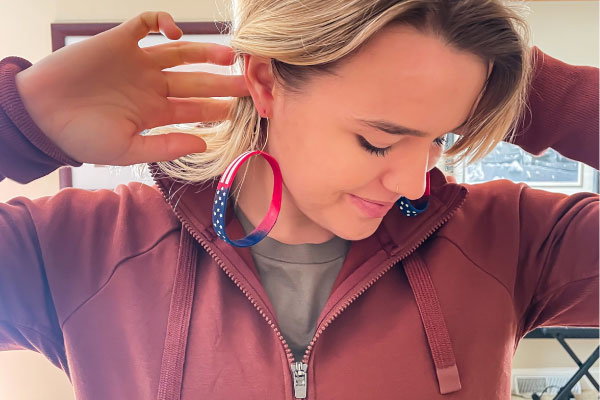 a model pulling her hair back wearing two american flag wristbands as earrings. 