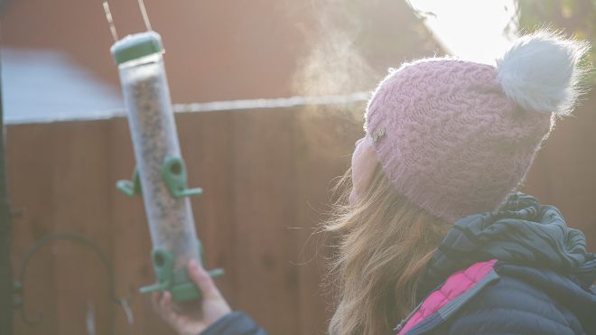 A bobble-hatted woman on a chilly day, placing a bird feeder in the garden