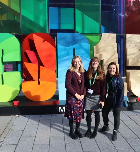 Three RSPB delegates at the UN biodiversity conference, COP15. A brightly coloured COP15 sign is behind them