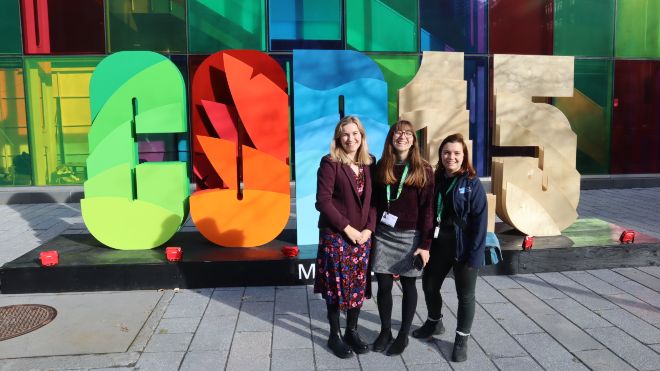 Three RSPB delegates at the UN biodiversity conference, COP15. A brightly coloured COP15 sign is behind them