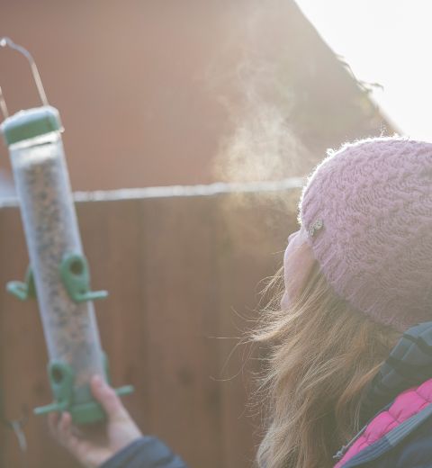 A bobble-hatted woman on a chilly day, placing a bird feeder in the garden