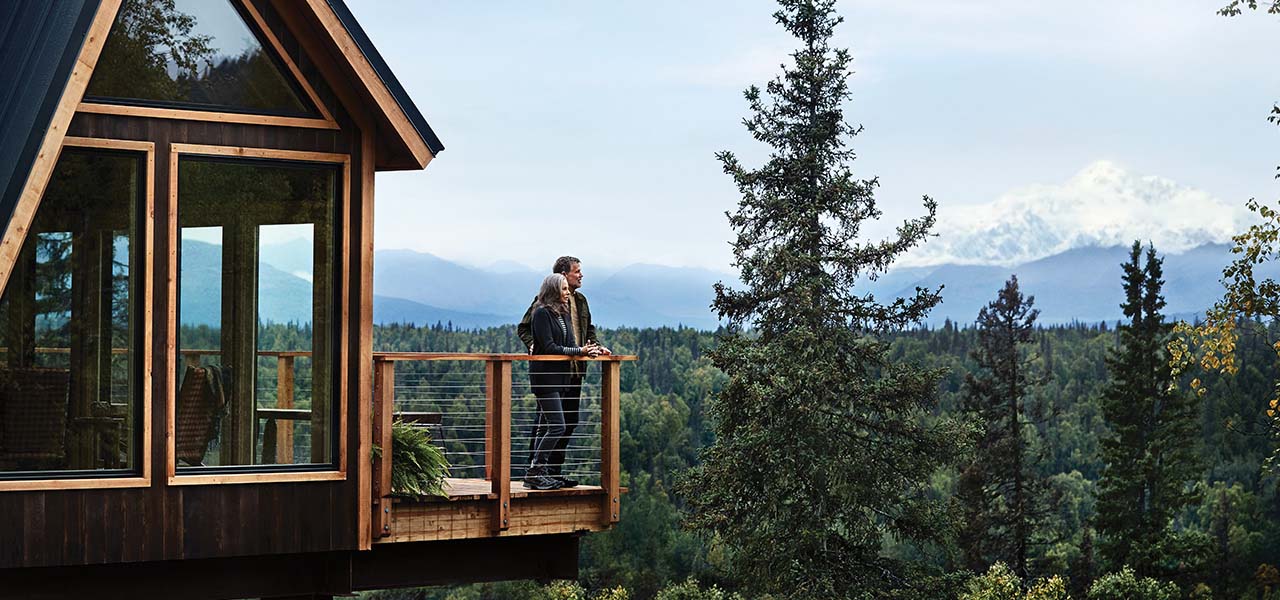 A couple on the balcony of a treehouse in Alaska. View 10-Night Alaska Cruisetours now.