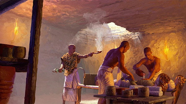 A drawing showing the inside of an underground embalming workshop in ancient Egypt. Soft light falls through a rectangular hole in the ceiling,and torches mounted on the wall illuminate two men with shaved heads wearing white wrap skirts, who stand on either side of a table adorned with lion heads. They are focused on mummifying a dead body, one of them wrapping the body’s arm with a cloth bandage, the other pouring a liquid from a pot over the bandaged torso. In the background, another man in a white wrap skirt and a loose colourful tunic shirt looks like he’s burning incense on a small, shallow bowl with a long handle. 