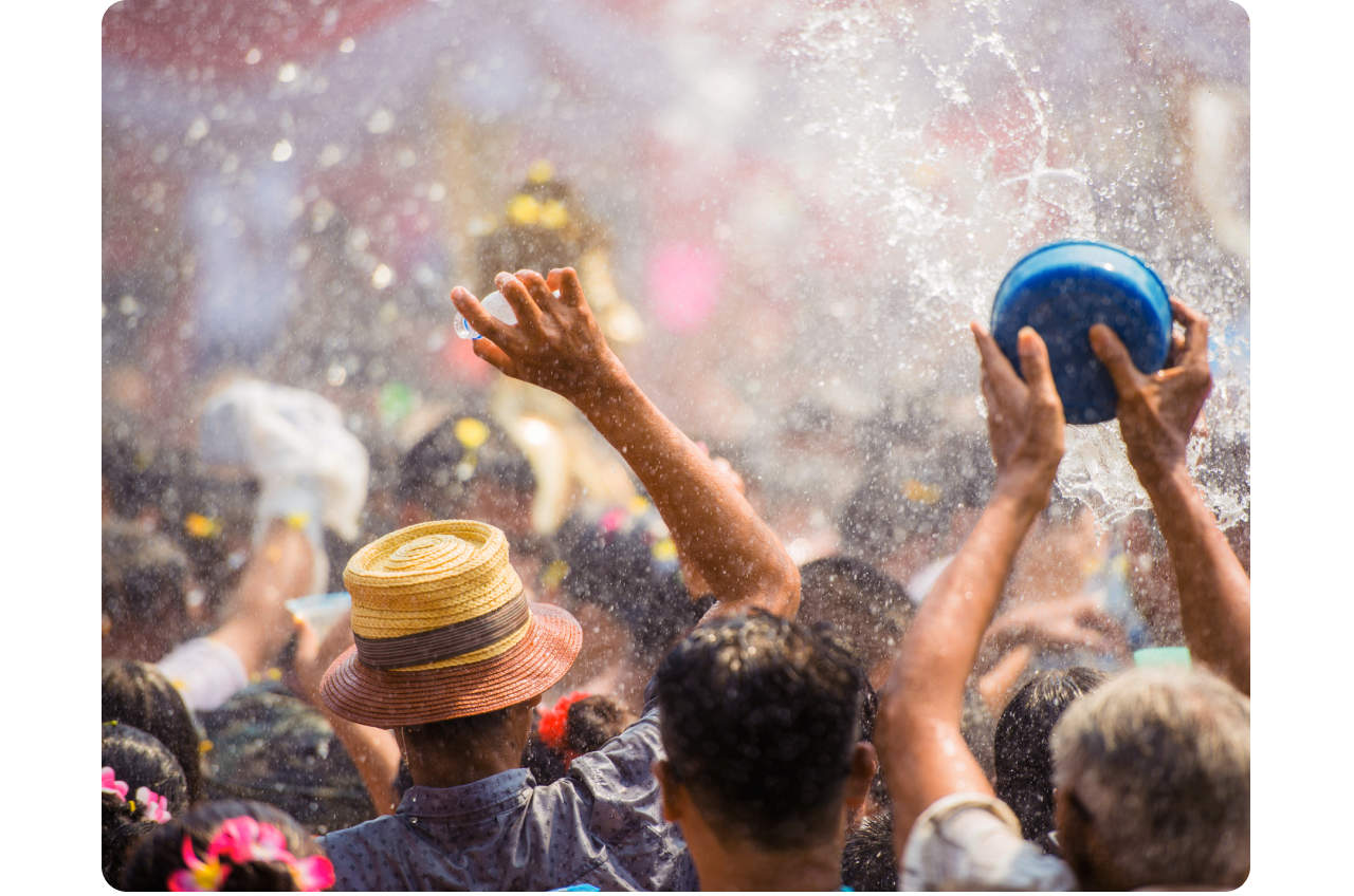 Thailand’s Songkran festival. A large group of people face away from us, arms raised, holding buckets and bottles that send water everywhere, drenching everyone.