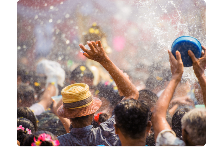 Thailand’s Songkran festival. A large group of people face away from us, arms raised, holding buckets and bottles that send water everywhere, drenching everyone.