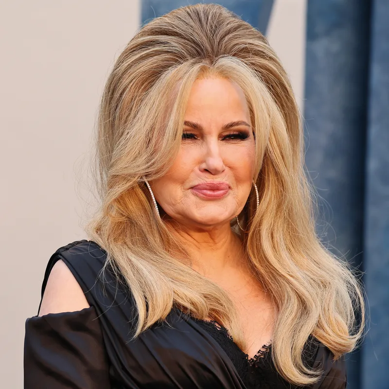 Jennifer Coolidge appears at the Vanity Fair Oscar party in a black dress. Her hair is worn in a half-updo with lots of volume.