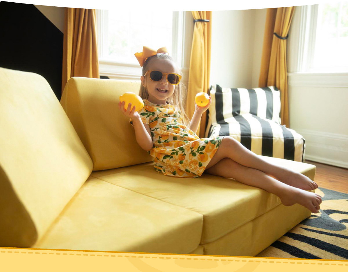 A child sits on their Lemonade Nugget holding two lemons.