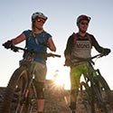 Zwei Personen stehen mit dem Bike bei Sonnenuntergang auf eine Kiesvorplatz