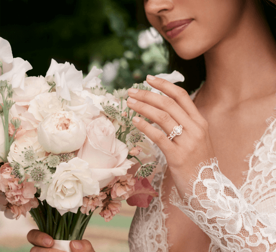 Close up of a woman in her bridal dress admiring a bouquet of flowers, with wedding ring prominently displayed.