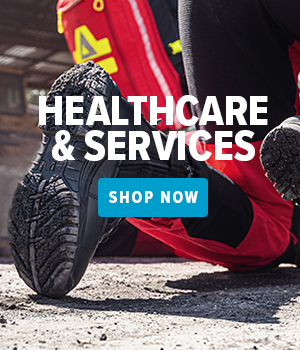 Person wearing a healthcare uniform, kneeling on the ground and showing the outsoles of their boots