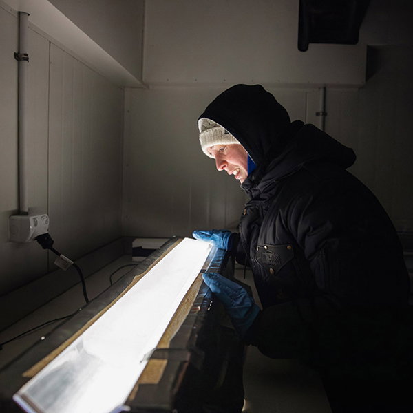 A person bundled up in winter clothes gazes at a brightly lit ice core.
