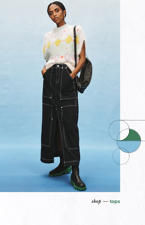 Woman in long denim skirt and printed sweater vest. Shop tops.