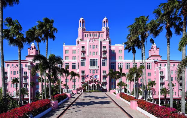 The exterior of the Don CeSar hotel in St. Pete, Florida reveals a grand pink palace featuring a palm-tree-lined entrance.