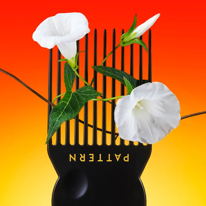 still life image of upside down Pattern hair pick with white flowers on bristles in front of a gradient orange and yellow background