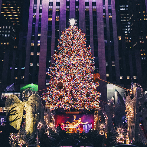 Image Description: A brightly-lit Christmas tree in front of Rockefeller Centre