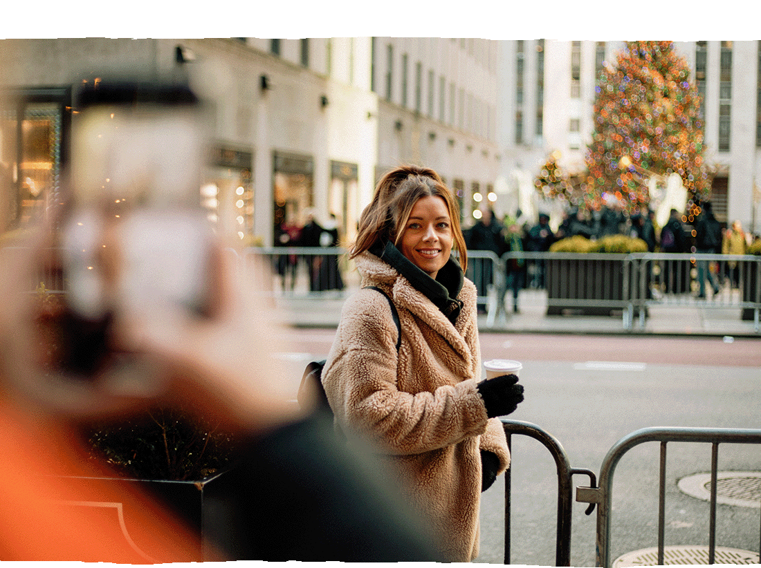 Image Description: A traveller posing for a photo with a Christmas tree in the background in New York City
