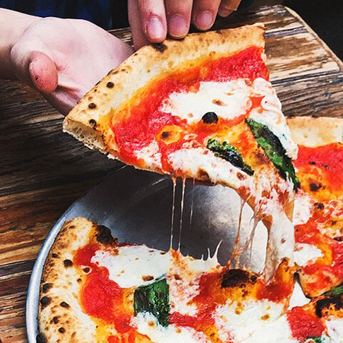 Image Description: A traveller grabbing a slice of fresh Pizza Margherita