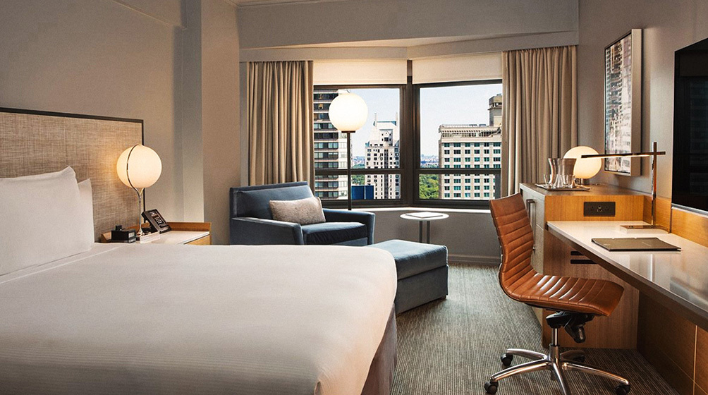 Image Description: A modern suite featuring a work desk, a cosy sitting area, and a skyline view of Manhattan