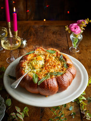 Giant stuffed squash on a plate, with candles and festive decor on the table 