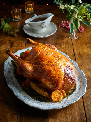 Roast turkey on a plate with gravy and festive decor to the back