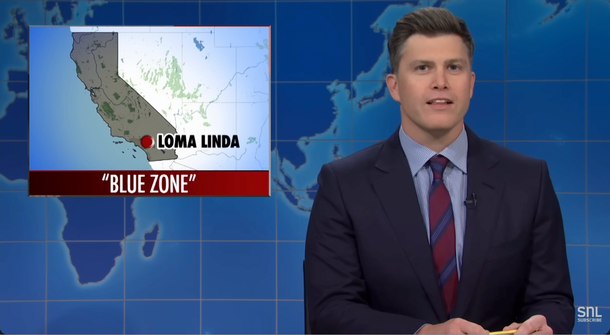 Colin Jost sitting at a table reading the news on Saturday Night Live's Weekend Update