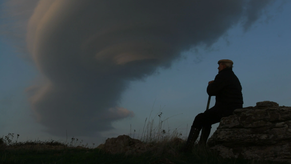 a man sitting on a rock with a cloud in the sky
