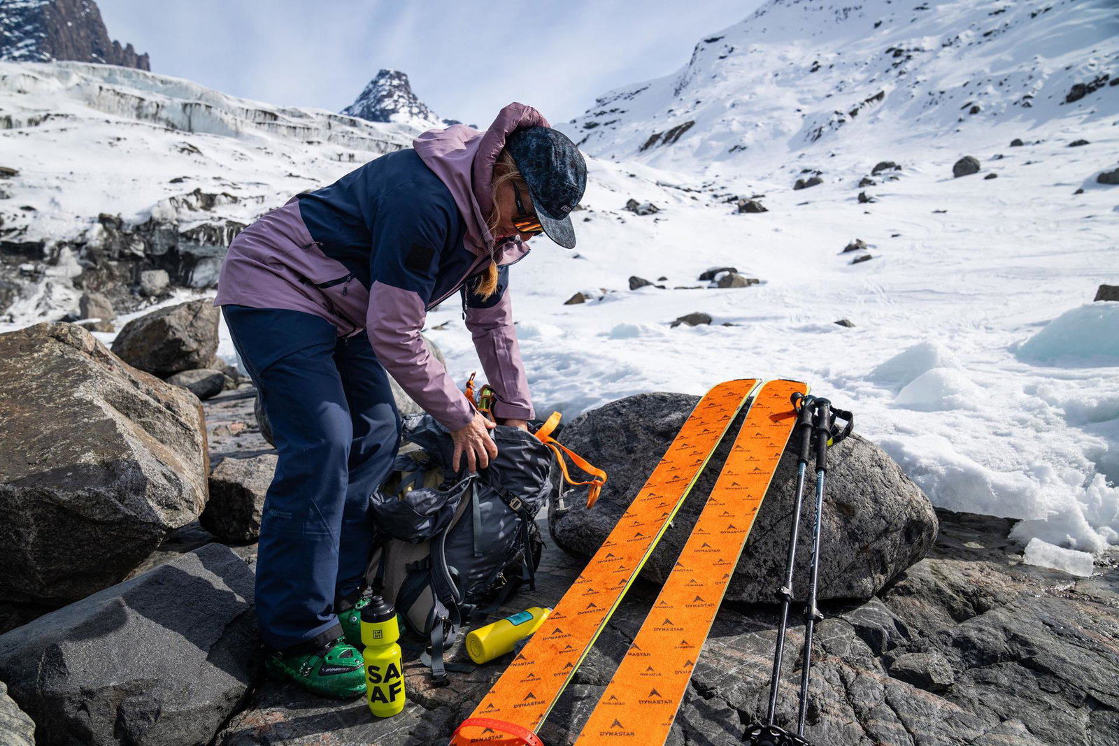 A woman on a mountain with skis and poles beside her, and she's reaching in her backpack.